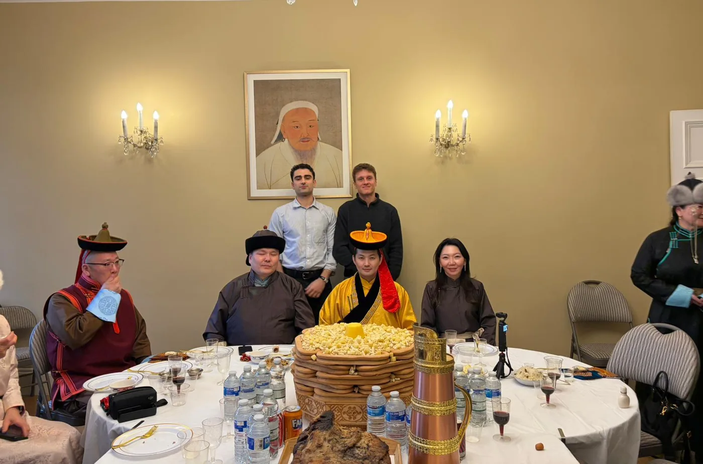 The two founders standing behind a table laid for a traditional Mongolian celebration, with guests in traditional deel robes and a tall tower of ul boov pastries at the centre